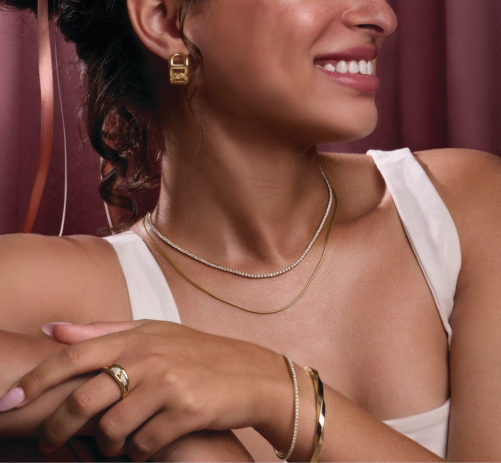 Woman wearing a 14K yellow gold necklace, earrings, and bracelet with a neutral background.